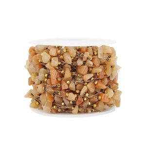 Detail of natural orange stone bead chain with gold square spacers on a white spool