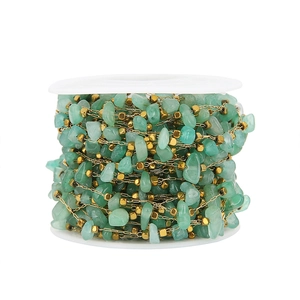 Detail view of green raw stone and gold square bead chain on a white plastic spool