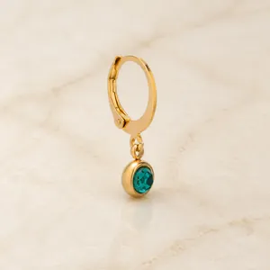 Detail of gold ear clip accessory with a clear green gemstone pendant in bezel setting