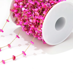 Detail of rose red stone bead chain with gold metal links on a white plastic spool