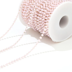 Detailed macro of pink faceted crystal beads with golden chain on a white spool
