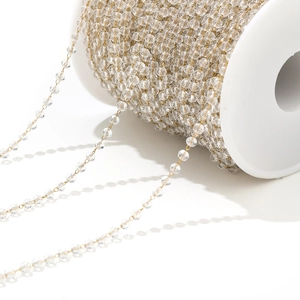 Macro detail of transparent crystal beads on a golden chain wound on a white spool