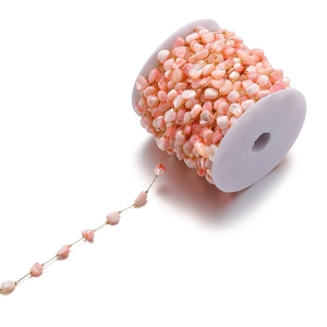 Detail of 7mm colorful shell beads and gold stainless steel chain on a white spool