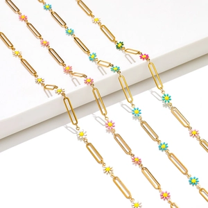 Macro shot of 18k gold paperclip chain featuring colorful enamel daisy charms on white steps