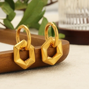 Orecchini a sospensione esagonali dorati su vassoio di legno scuro con foglie verdi decor