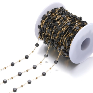 Detalle de cadena de acero inoxidable dorado con cuentas de cristal negro en carrete