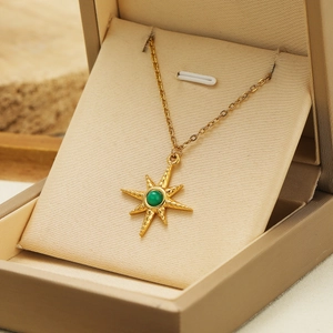 Gold eight-pointed star necklace with green gemstone pendant on beige jewelry box