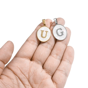 Close-up of oval gold and silver letter U and G pendants with white shell inlay for DIY jewelry