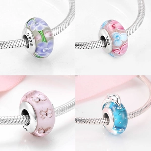 Macro detail of S925 silver core charms with floral and butterfly Murano glass patterns