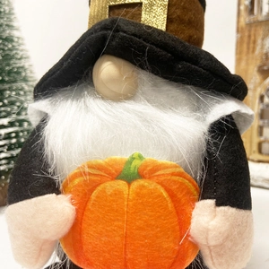 Close-up of harvest gnome with white beard holding a bright orange pumpkin ornament
