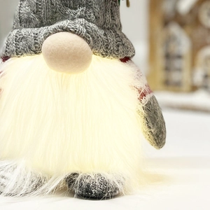 Close-up of lighted Christmas gnome with warm glowing beard and grey knitted hat decoration