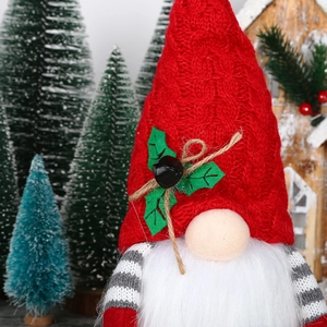 Detail of Christmas gnome with red knitted hat, green holly leaf, and bell decoration