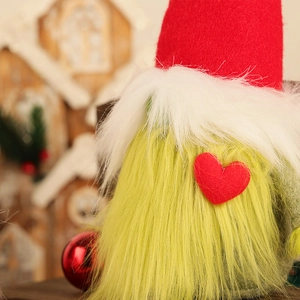 Christmas gnome doll with red heart, green beard and felt hat on festive wood background