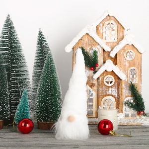 Close-up of white plush Christmas gnome with festive miniature tree background