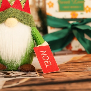 Close-up of a green felt Christmas gnome doll holding a red NOEL holiday gift tag