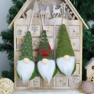 Three green forest Christmas gnomes with knitted hats hanging on a festive wooden backdrop