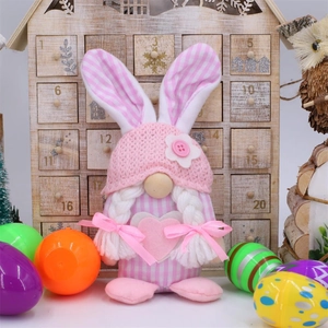 Pink plush Easter gnome with rabbit ears and colorful eggs on a wooden background
