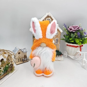 Detail of Easter gnome featuring orange knitted hat with bunny ears holding a pink egg