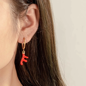 Boucles d'oreilles créoles dorées avec pendentif corail rouge sur l'oreille du mannequin