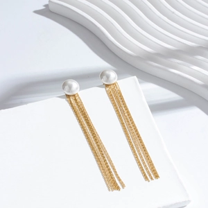 Orecchini a nappa dorati con perle bianche e lunghe catenelle su supporto minimalistico
