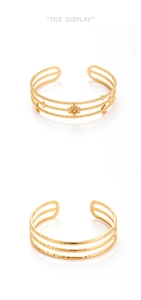 Dettaglio di bracciali rigidi dorati a strati con catene a sfere e motivo a sole