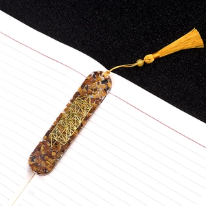 Oval resin bookmark with tiger eye stones, gold star inlay and yellow tassel on notebook