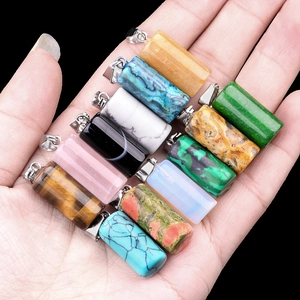 Polished natural crystal cylinder pendants with silver bails held by hand against black background