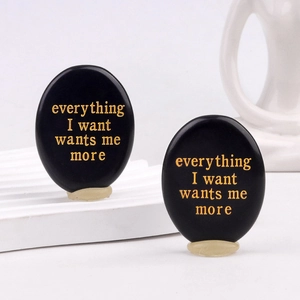 Oval black obsidian thumb stones with gold engraved motivational quotes on white platform