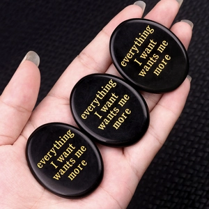 Polished oval obsidian stone with gold engraved phrase everything I want wants me more