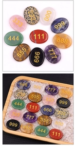 Macro shot of oval crystal palm stones with engraved gold angel numbers in a wooden tray