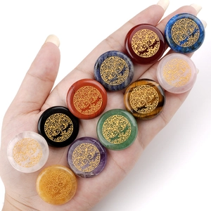 Hand holding 25mm natural crystal stones with golden Tree of Life engraved patterns