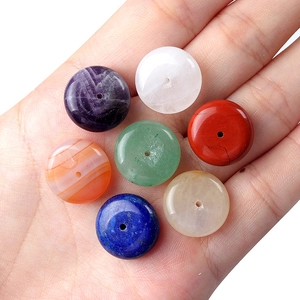 Set of seven colorful natural healing crystal donut pendants held in a person's palm