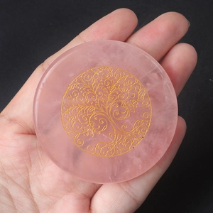 Mano sosteniendo un disco de cuarzo rosa con grabado dorado del árbol de la vida energético
