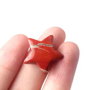 Polished red jasper star-shaped gemstone bead held between fingertips for DIY jewelry