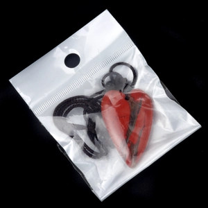 Roter Naturstein-Herzanhänger mit Kordel in transparenter Verpackung auf schwarzem Grund