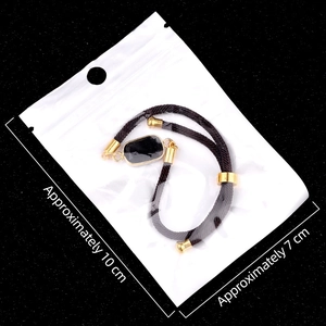 Adjustable black cord bracelet with gold-framed rectangular stone in retail packaging