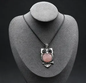 Detail view of owl pendant with pink crystal belly on retro silver metal and black cord