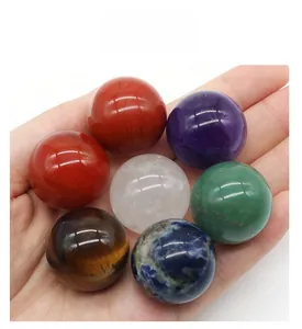 Macro view of seven assorted 25mm natural crystal chakra spheres held in a palm