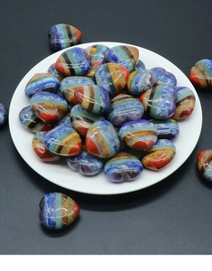 Close-up of polished heart-shaped chakra stones with colorful stripes in a white ceramic dish