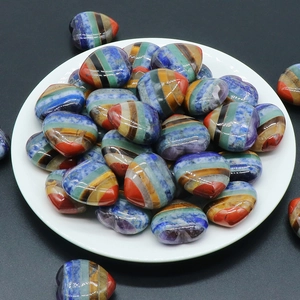 Polished heart-shaped natural crystal chakra stones stacked in a white dish on black background