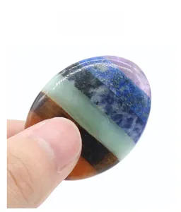 Detailed view of a multi-layer seven chakra worry stone held by fingers for size reference