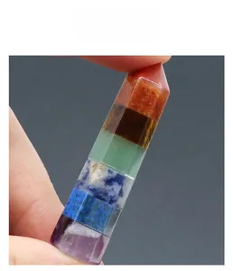 Detailed close-up of a hand holding a 7 chakra hexagonal stone column showing layered crystals