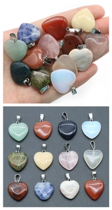 Various natural crystal heart pendants held in palm and arranged on grey background