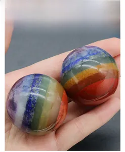 Close-up of hand holding a polished seven-chakra natural gemstone sphere ornament