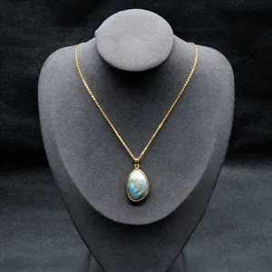 Gros plan du pendentif en labradorite bleue sur chaîne dorée sur fond texturé gris foncé