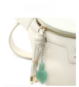 Detail of a white leather bag featuring a light gold zipper and green jade-like pendant