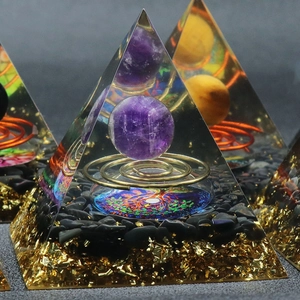 Orgone energy pyramid with amethyst sphere, copper coil, and tree of life over black stones