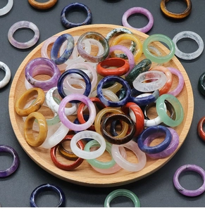 Variety of polished natural gemstone rings in amethyst, lapis, and agate on wood tray
