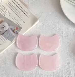 Detailed view of four cat-shaped natural rose quartz facial massage scrapers on white linen