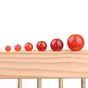 Polished red agate beads in various sizes for DIY jewelry making on wooden stand